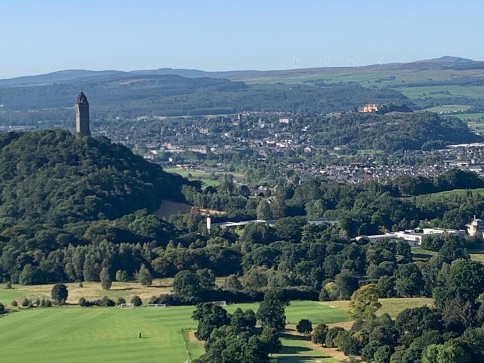 A panoramic view of a town with a prominent tower on a hill, surrounded by lush greenery and a mix of residential and commercial buildings.