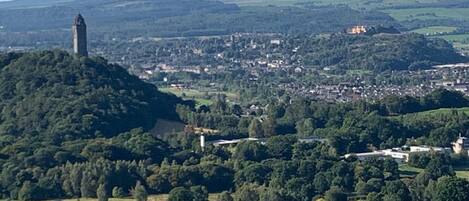 A panoramic view of a town with a prominent tower on a hill, surrounded by lush greenery and a mix of residential and commercial buildings.