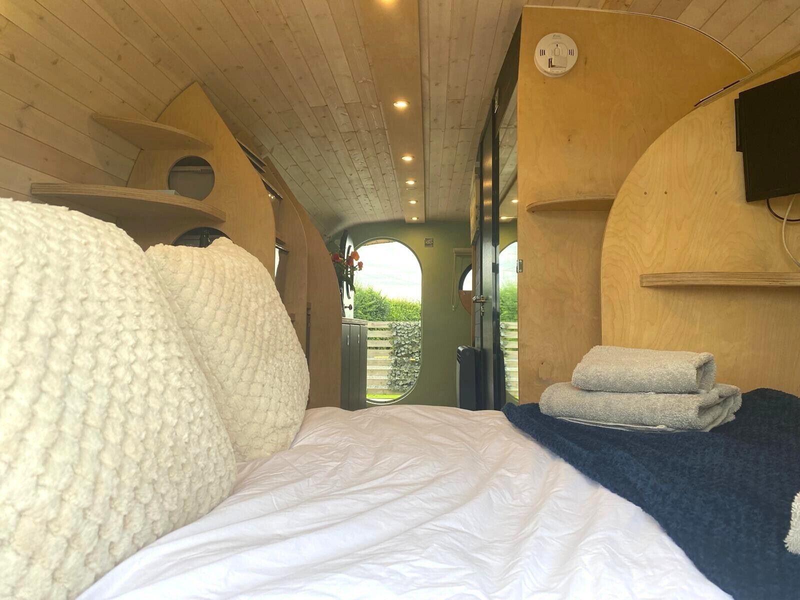 A cozy room with a bed, a wooden ceiling, and a view through an open door.