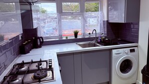 Une cuisine moderne équipée d’une cuisinière à gaz, d’un lave-linge encastré et d’une fenêtre agrémentée de rideaux décoratifs.