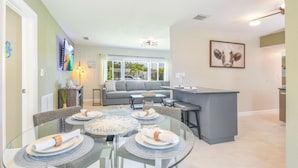 A modern kitchen with a central island, dining area with round glass tables, and a living area with a sofa and large windows. - Private HEATED Pool • Newly Renovated • 5 minutes to the Beach (Seminole)