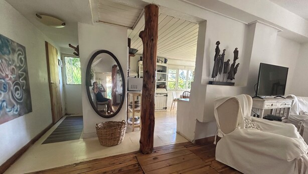 A room with wooden flooring, a large mirror, a wicker basket, a white sofa, and a television on a stand.