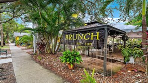 A covered outdoor seating area labeled "BRUNCH sat - sun" with a sign, surrounded by trees and plants. - GUEST HOUSE w/ PRIVATE ENTRANCE & PATIO for rent in Gulfport, FL (Gulfport)