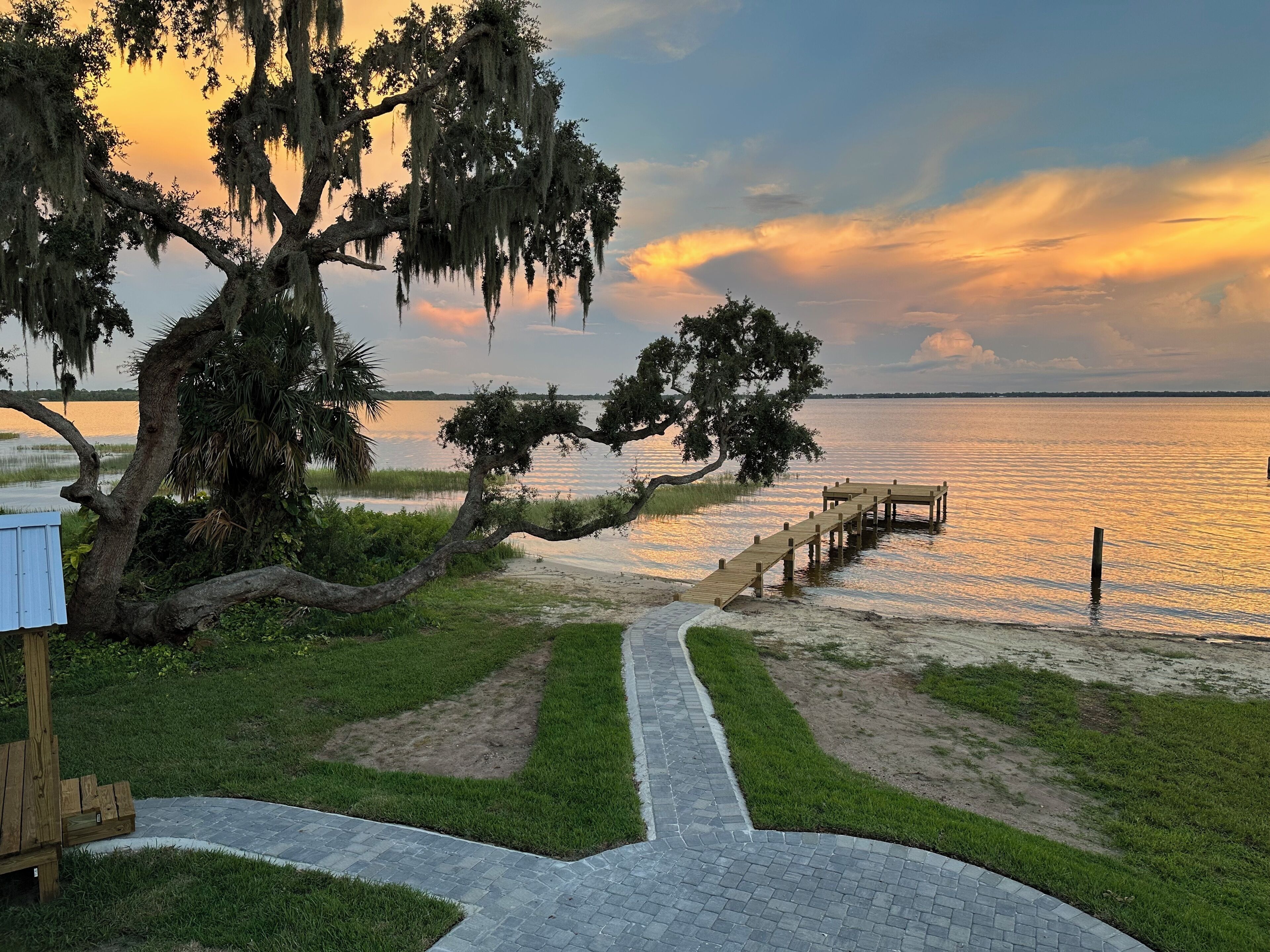 A wooden deck leading to a dock over water, surrounded by grass and trees.