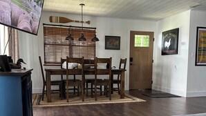 A spacious living room with a wooden dining table, a sofa, and a TV mounted on the wall.