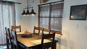 A dining area with a wooden table and chairs, a woven rug, and a ceiling fan.