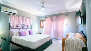 Un dormitorio con cama, escritorio, silla, televisor y aire acondicionado.