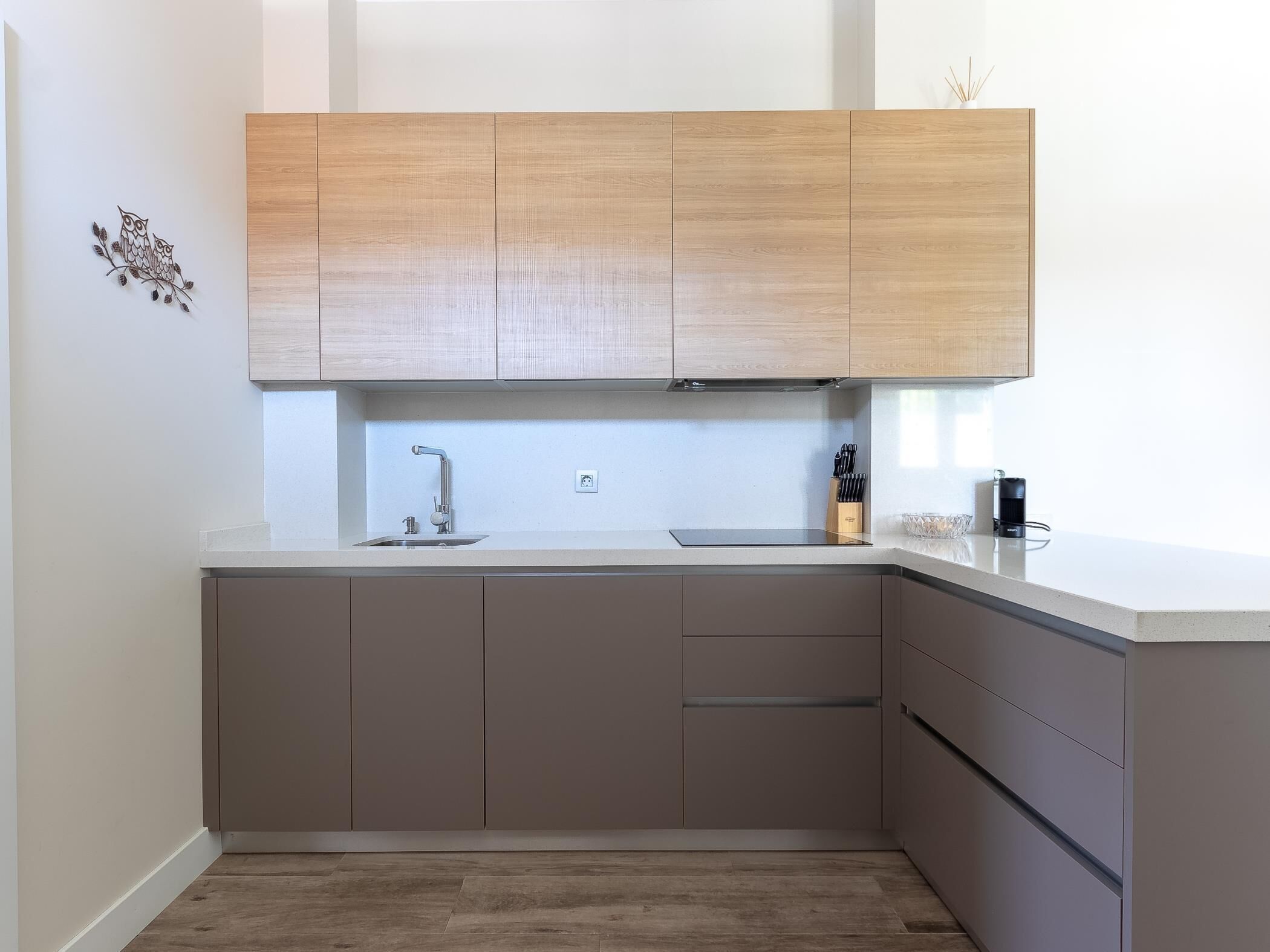 Ett modernt kök med ljusa träskåp, en diskho i rostfritt stål och en bänkskiva med ett knivblock och en kaffemaskin.