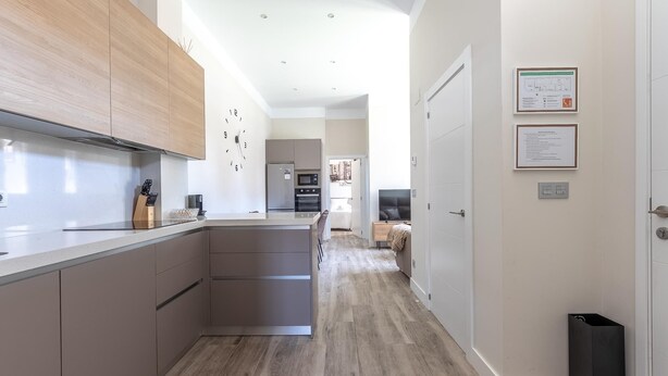 A modern kitchen with a central island, wooden cabinets, and a built-in oven. - Hospital Cruces Metro Bec (Barakaldo)