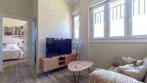 A modern living room with a flat-screen TV, a wooden entertainment unit, a round coffee table, and a sofa. - Hospital Cruces Metro Bec (Barakaldo)