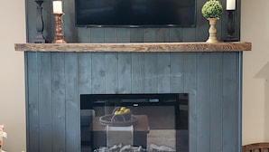 A living room with a flat-screen TV mounted above a fireplace, a wooden mantel, and a seating area with a couch.
