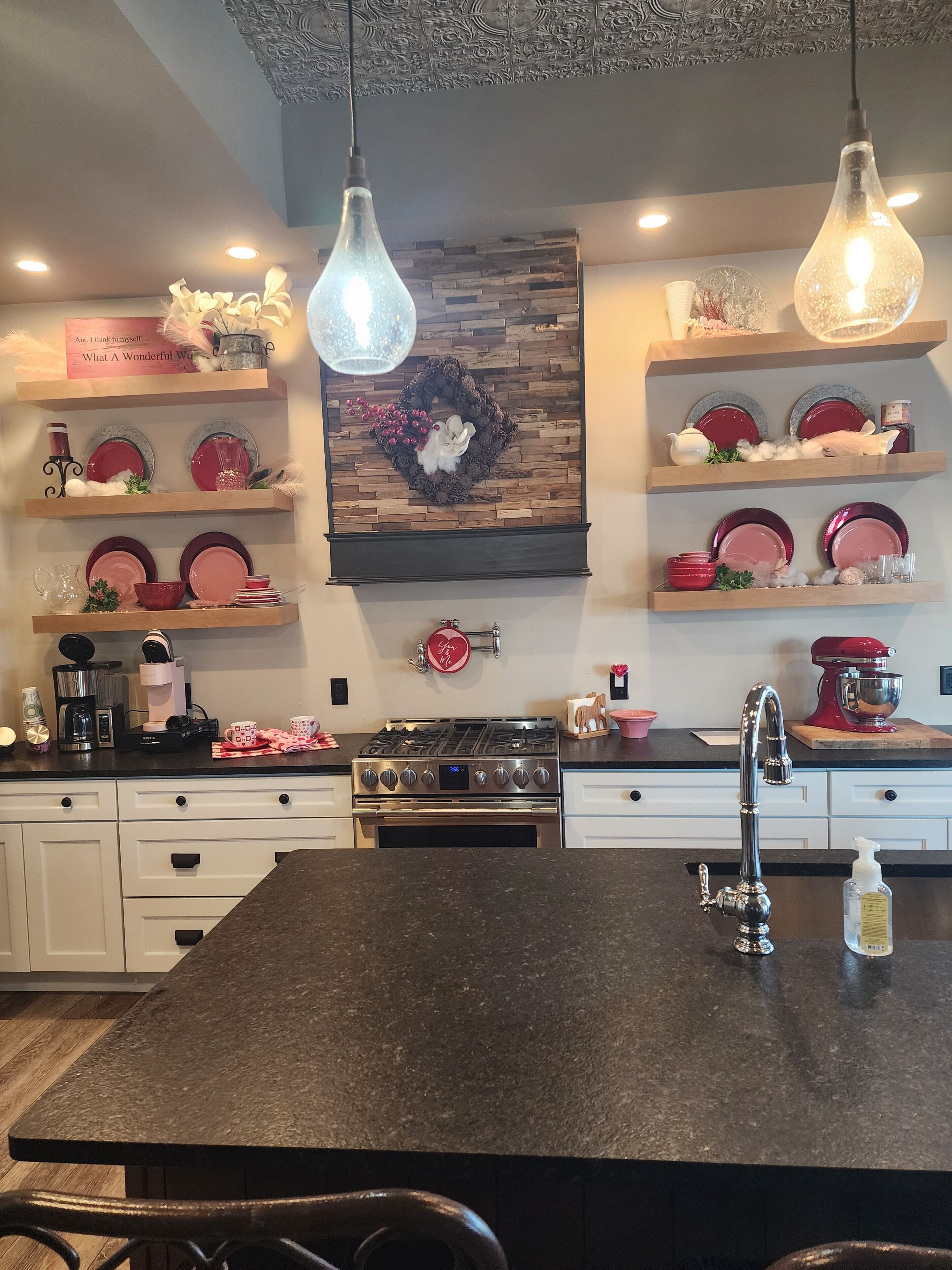 A modern kitchen with a central island, stainless steel appliances, and decorative wall shelves.
