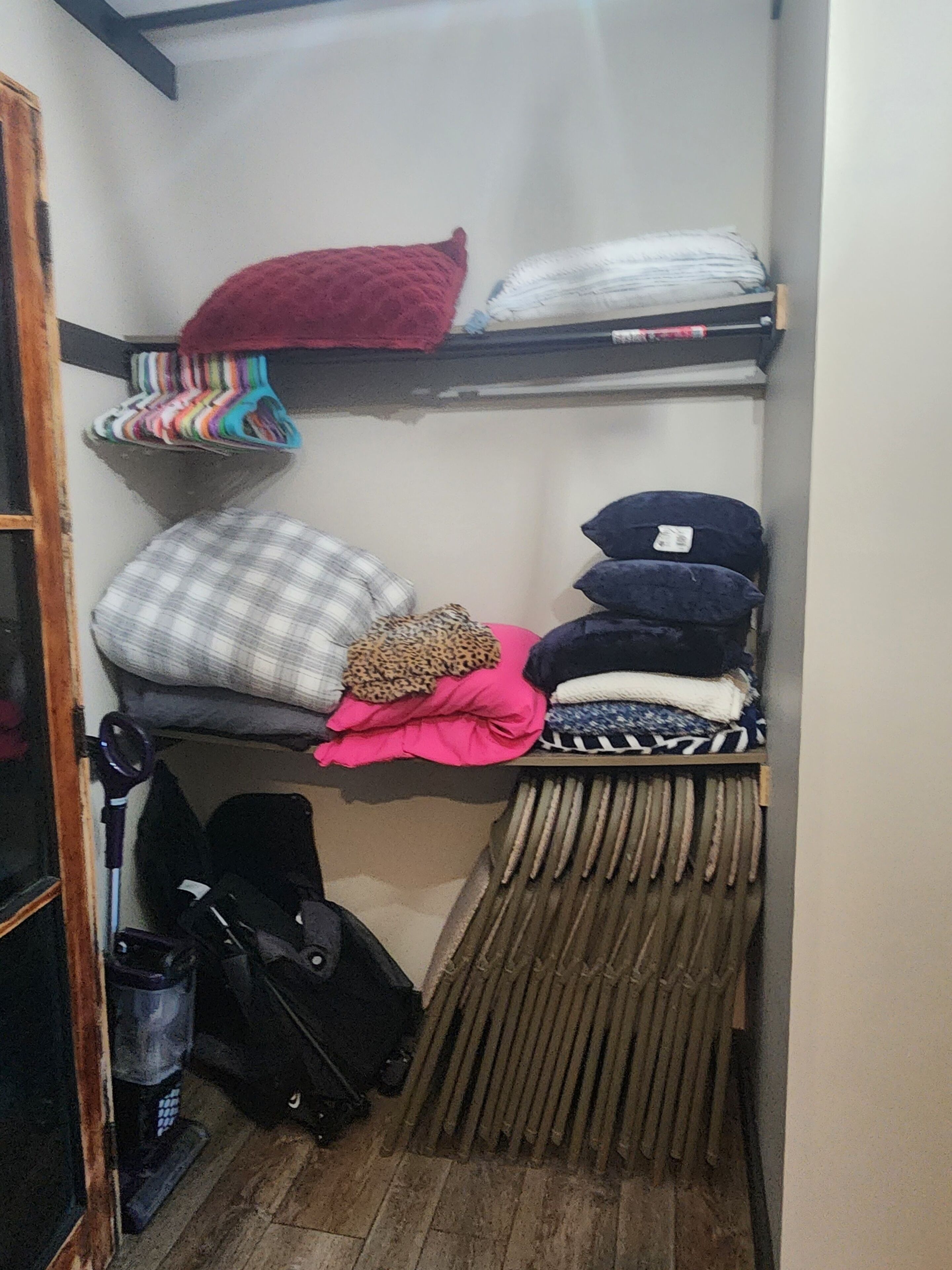 A small, narrow storage space with shelves holding various folded items, including pillows and blankets.