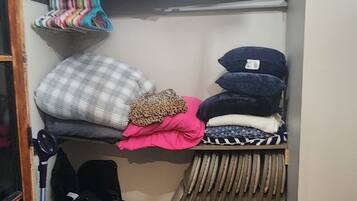 A small, narrow storage space with shelves holding various folded items, including pillows and blankets.