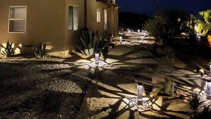 A desert-style building with a flat roof and minimalistic design, surrounded by landscaped areas with cacti and other desert plants.
