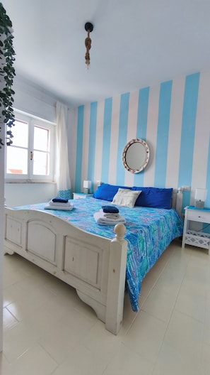 A bedroom with a bed, a bedside table, a nightstand, a mirror, and a window with curtains.