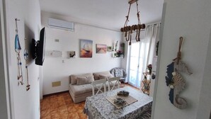 Una sala de estar con un sofá, una mesa de comedor y un televisor montado en la pared.