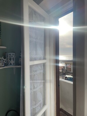 Una habitación con ventana que da a la costa, una puerta blanca y un estante con objetos decorativos.