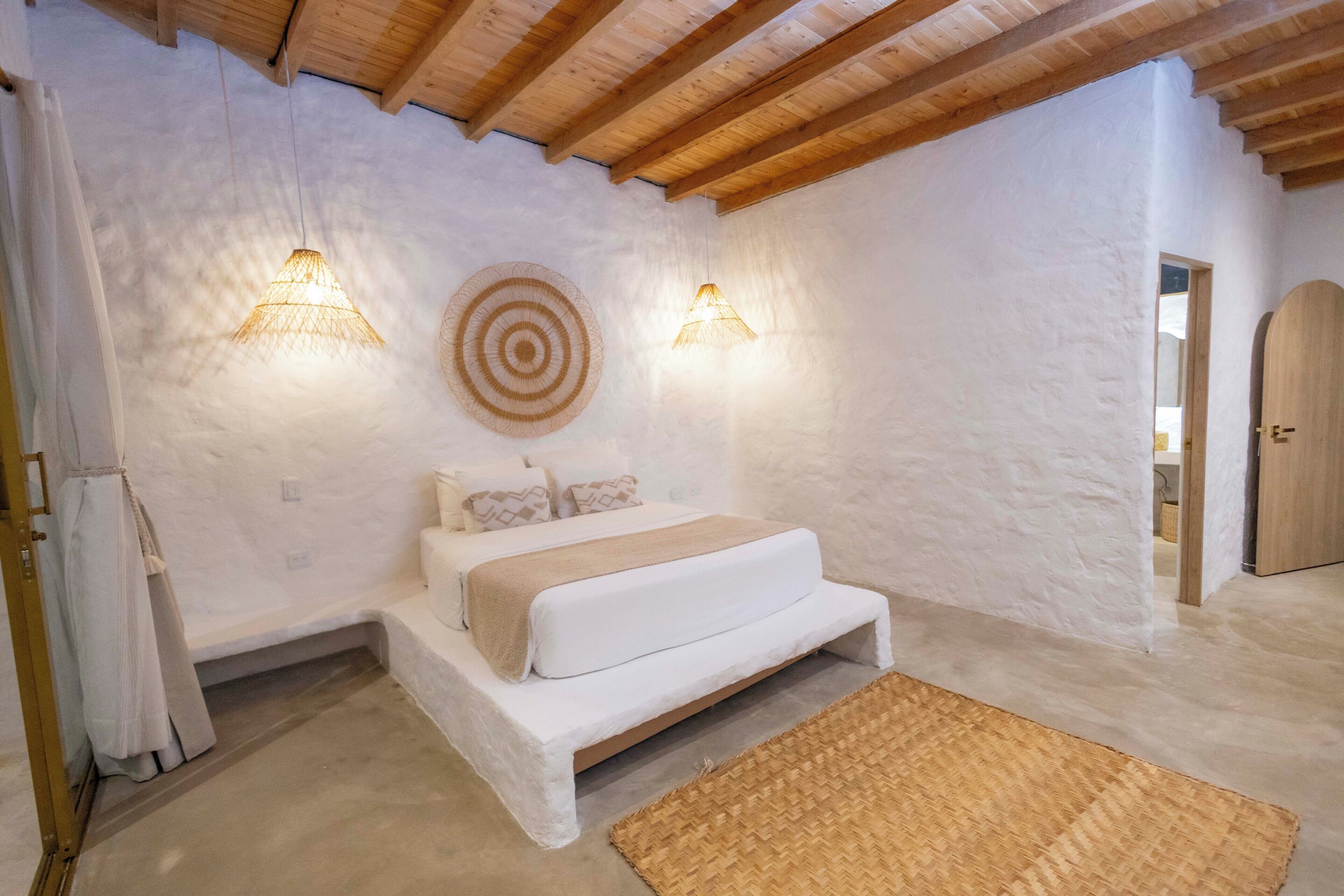 A bedroom with a bed, two wall-mounted lights, a woven rug, and a wooden door.