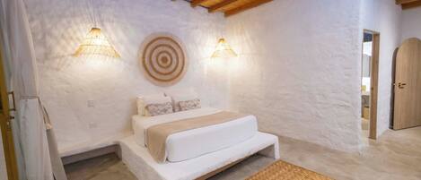 A bedroom with a bed, two wall-mounted lights, a woven rug, and a wooden door.