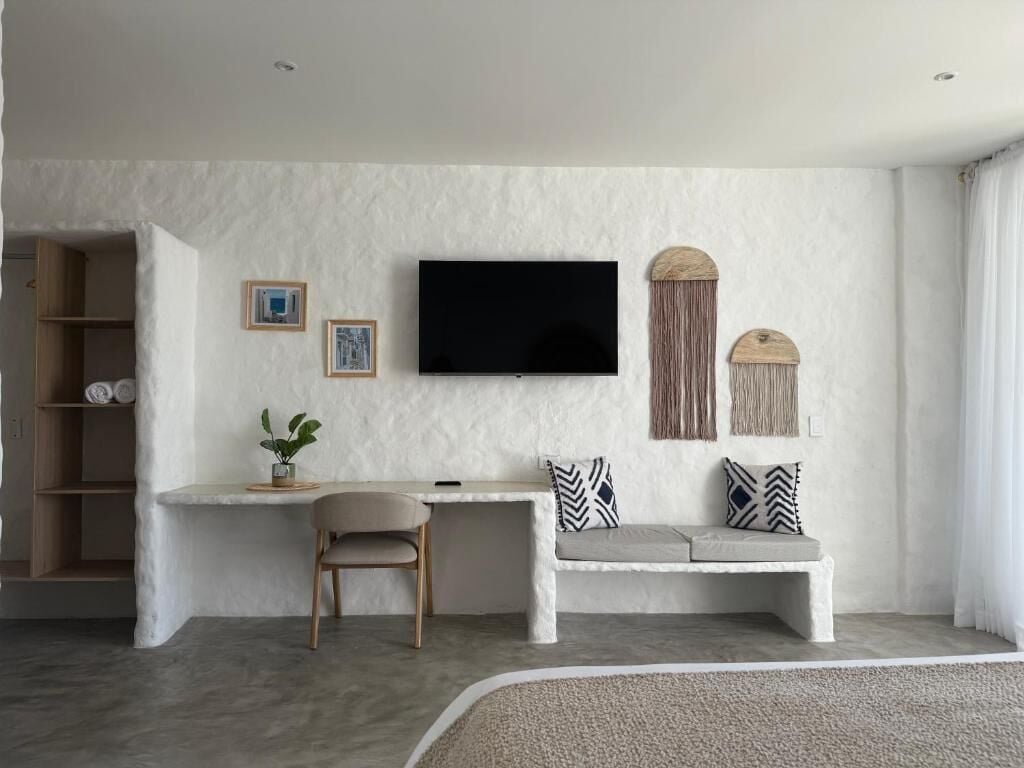 A modern living room with a flat-screen TV, a sofa with patterned cushions, a small table with a chair, and a plant.