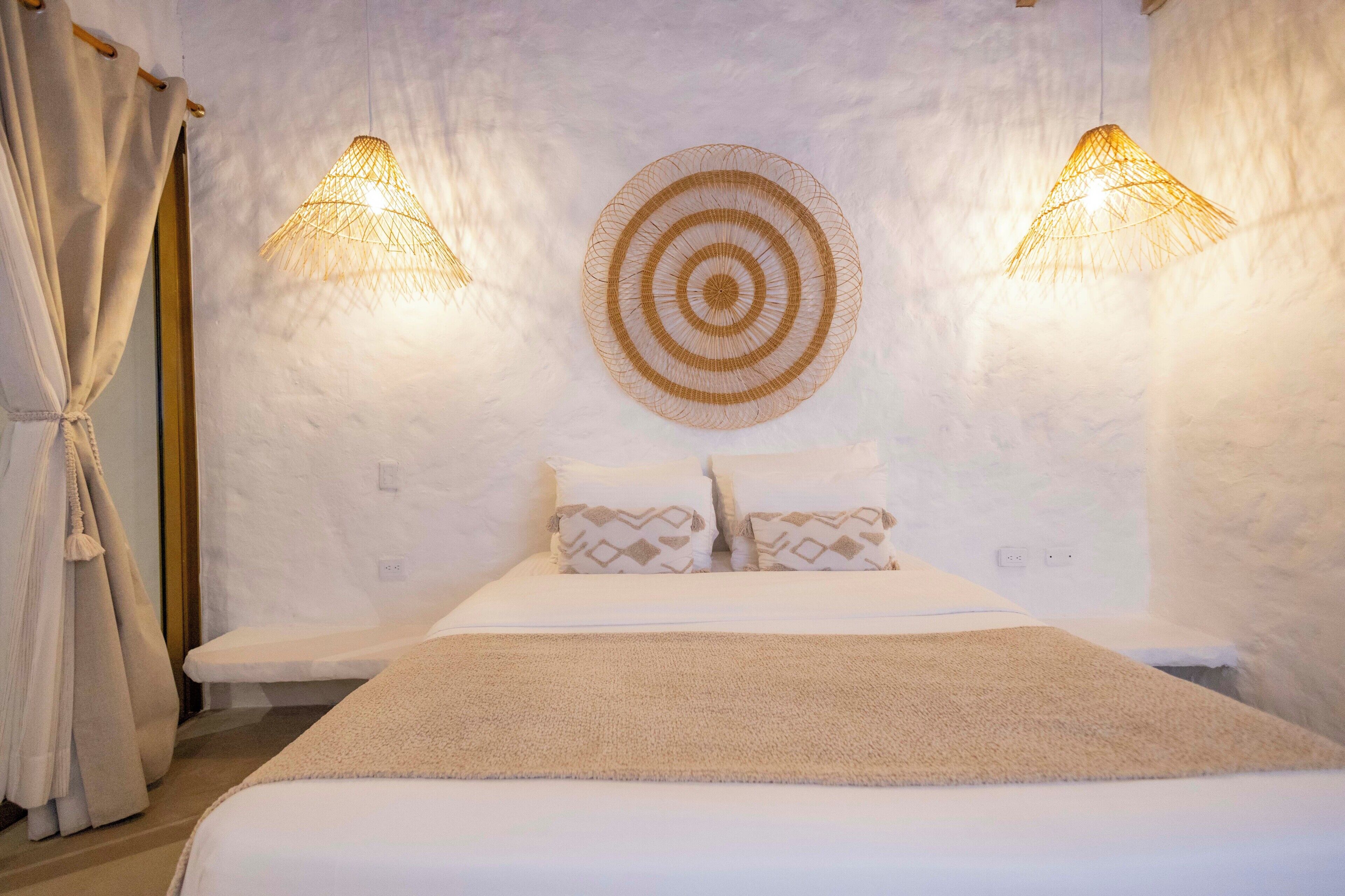 Un dormitorio con cama, dos lámparas de pared, un adorno circular en la pared y un banco.