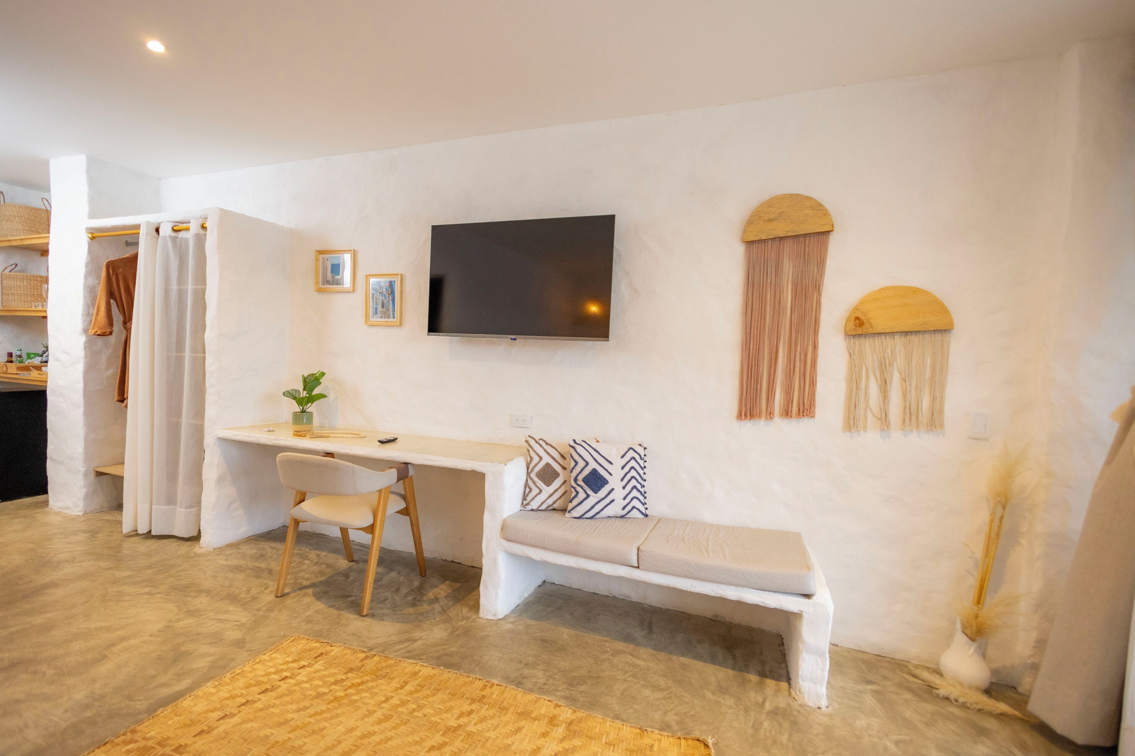 Una sala de estar moderna con un televisor de pantalla plana, un sofá blanco, un escritorio con una silla y un banco.