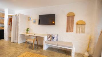 Una sala de estar moderna con un televisor de pantalla plana, un sofá blanco, un escritorio con una silla y un banco.