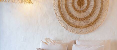 A bed with white bedding, a woven wall hanging, and a hanging light fixture.