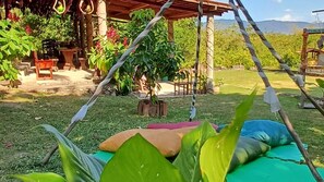 Una hamaca bajo una pérgola de madera con plantas en macetas y vistas a un paisaje montañoso.