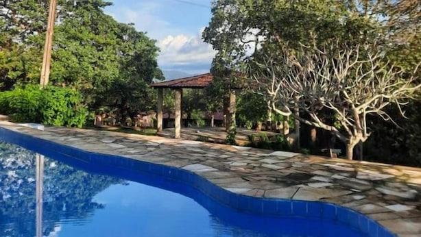 A swimming pool with stone tiles, surrounded by trees and a gazebo. - Sitio Pedagógico Vale da Serra (Maranguape)