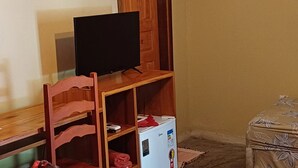 A room with a television on a wooden stand, a small white refrigerator, and a patterned sofa. - Sitio Pedagógico Vale da Serra (Maranguape)