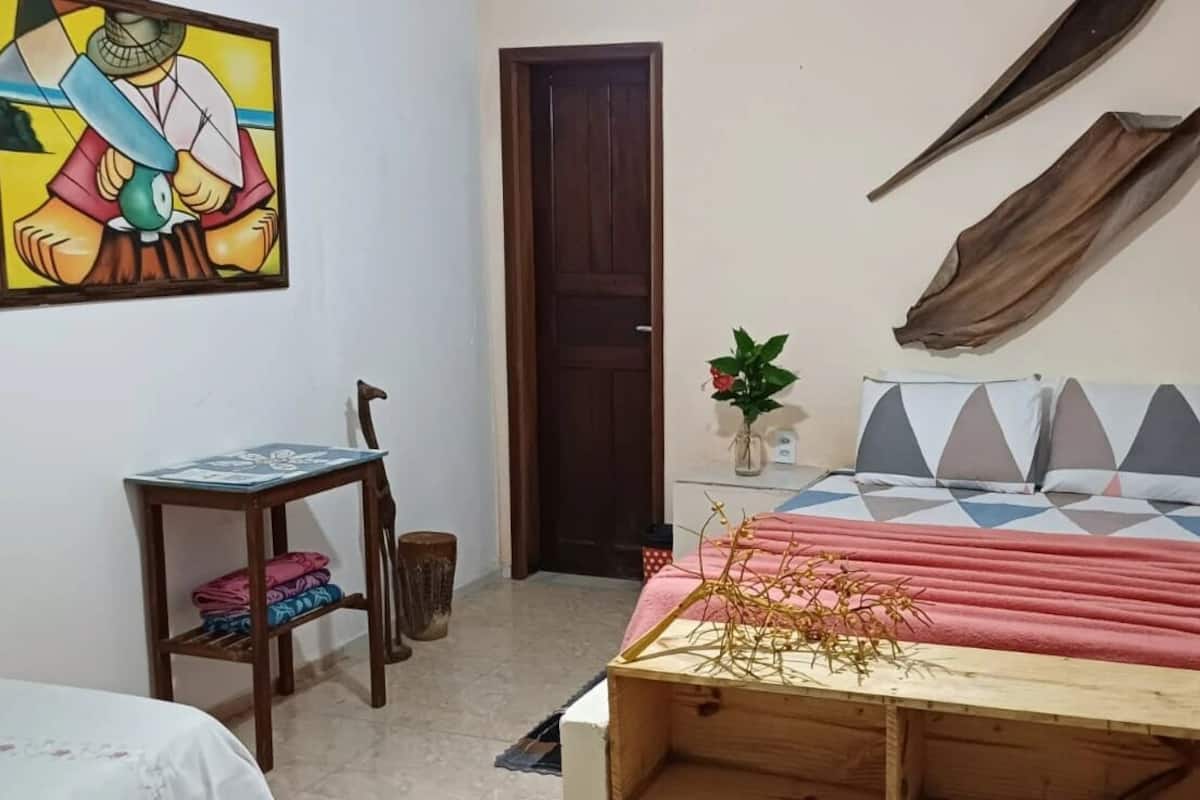 Une chambre à coucher comprenant un lit, une petite table, une chaise, une armoire en bois, une étagère fixée au mur et une porte.