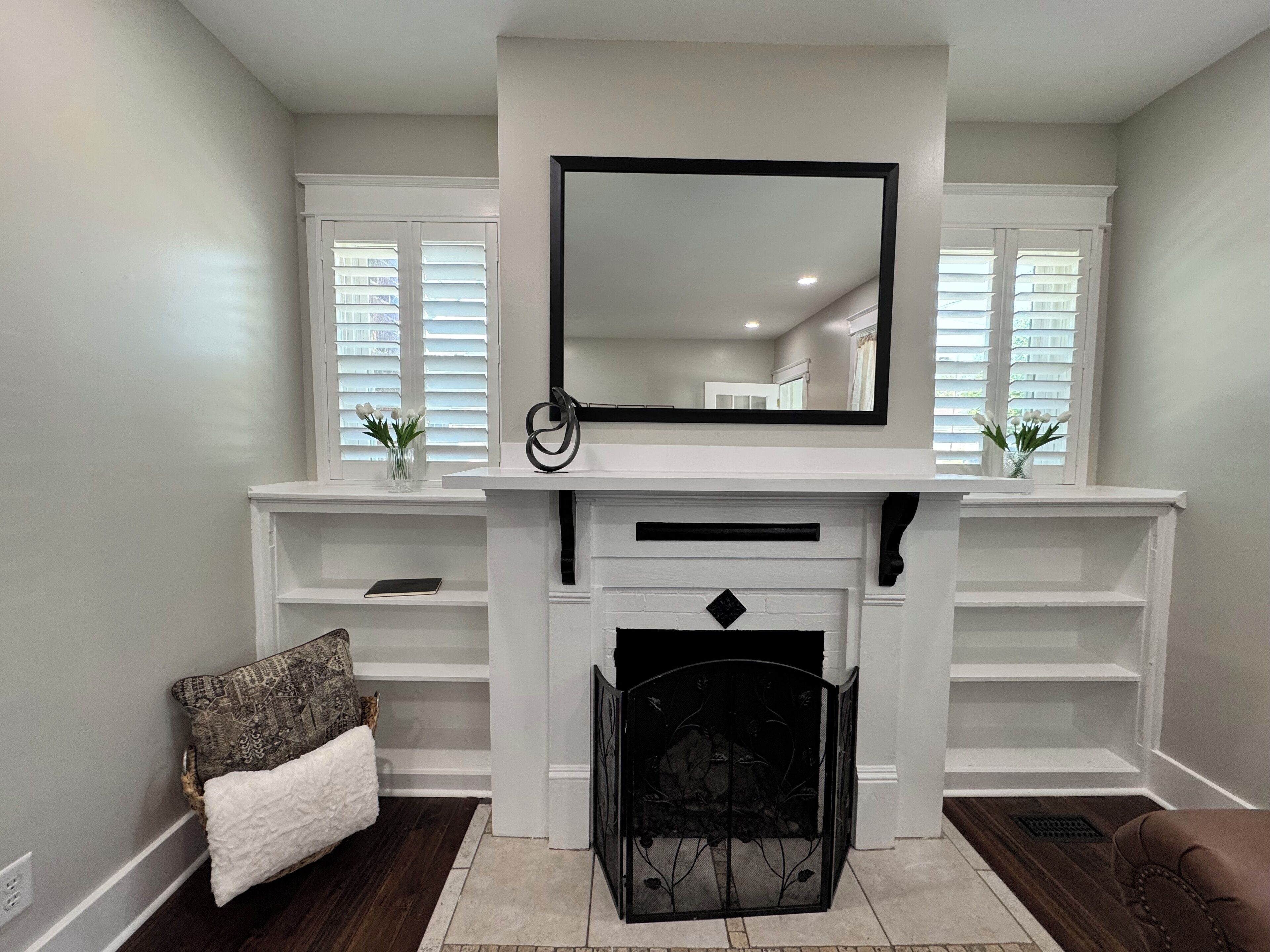 A living room with a fireplace, white walls, and a large mirror above it.
