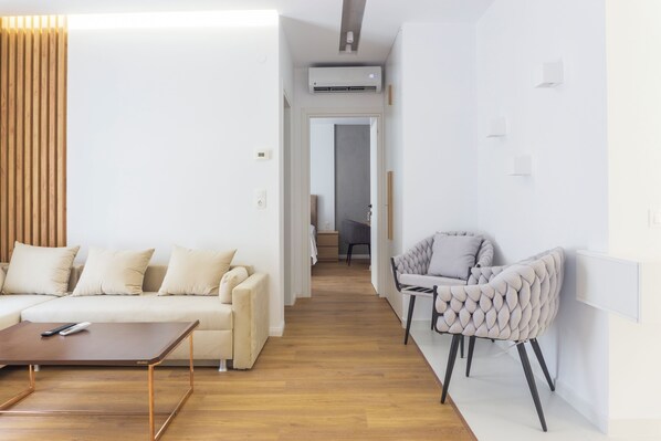 Una sala de estar moderna con un sofá, una mesa de centro y una silla. Se ve un pasillo que conduce a otra habitación.