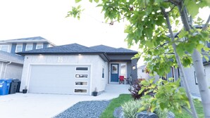 A modern two-story house with a garage, number 26, and a small front yard with a red chair and potted plants.