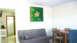 Un salon avec un canapé gris, une table à manger en bois et des chaises. Un tableau encadré représentant une tortue de mer est accroché au mur.