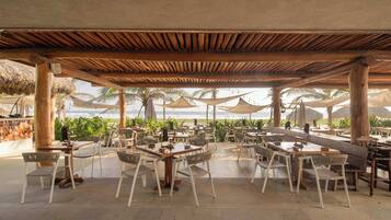 An outdoor dining area with tables and chairs, a wooden ceiling, and a view of the ocean.