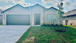 A residential house with a garage, a well-maintained lawn, and a clear sky. - Brand New home, 4 beds Bison Ridge Retreat Ft Sill (Lawton)