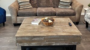 A living room with a brown sofa, a wooden coffee table, and a painting of flowers on the wall. - Brand New home, 4 beds Bison Ridge Retreat Ft Sill (Lawton)