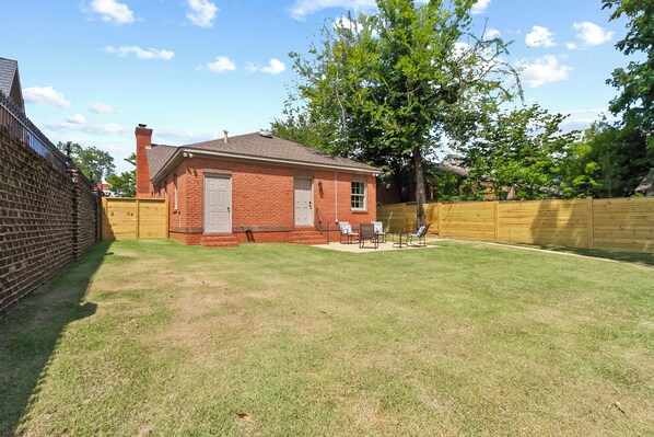 A small brick house with a fenced backyard, a tree, and a patio with outdoor furniture.