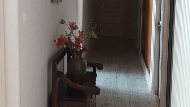 Een gang met een houten vloer, een bloemenvaas en een schilderij aan de muur.