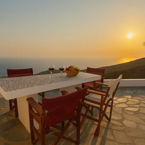 Une table dressée pour deux personnes, avec des verres à vin et un panier de fruits, offrant une vue imprenable sur un magnifique coucher de soleil.