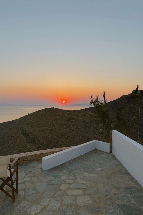 Une vue sur le coucher de soleil depuis une terrasse dallée de pierre, avec un mur blanc et une chaise en bois.