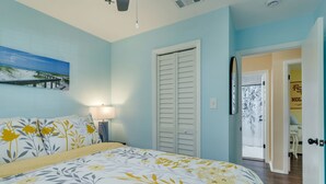 Un dormitorio con una cama, una mesita de noche, una lámpara, una puerta y un cuadro en la pared.