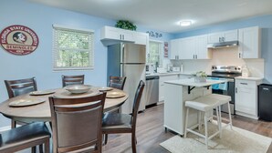 Una cocina moderna con armarios blancos, un refrigerador de acero inoxidable y un comedor con sillas de madera y una mesa redonda.