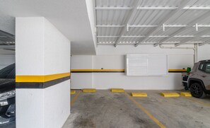 A parking garage with concrete floors, yellow and black painted lines, and a white wall with a vent. - Apartments in the Turquesa Building - Balneario Picarras - RTS (Picarras)