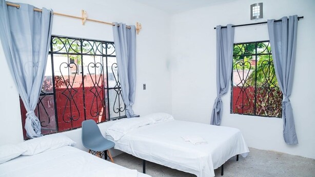 Une chambre avec deux lits simples, une chaise et une fenêtre avec des barreaux en métal.