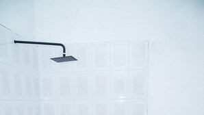 Une petite salle de bain carrelée, équipée d’une douche, de toilettes et d’un robinet mural.