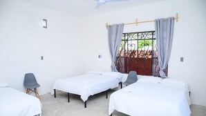 Une chambre avec trois lits simples, un ventilateur de plafond, une fenêtre avec des barreaux et une vue sur un jardin.